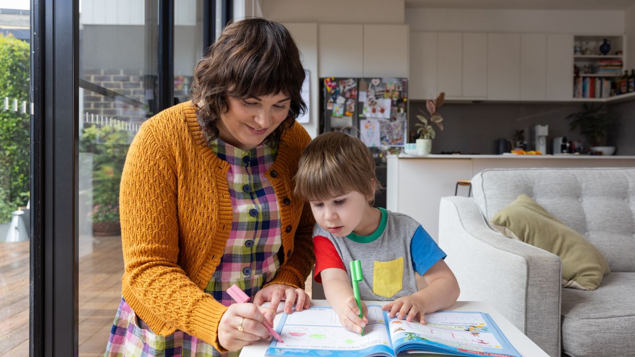 A mother colouring pages with her child in their lounge room